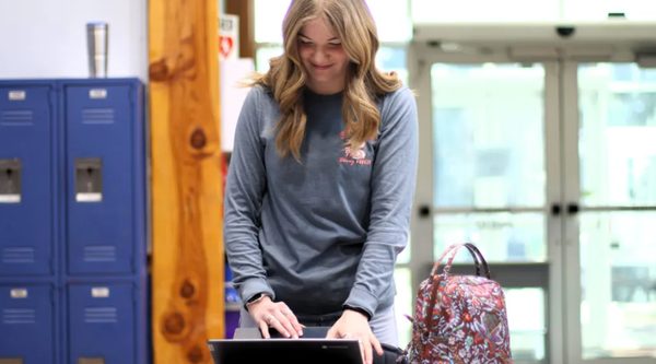 Faith Dudley, a Concord Christian Academy junior, standing at her laptop in the school hallway.